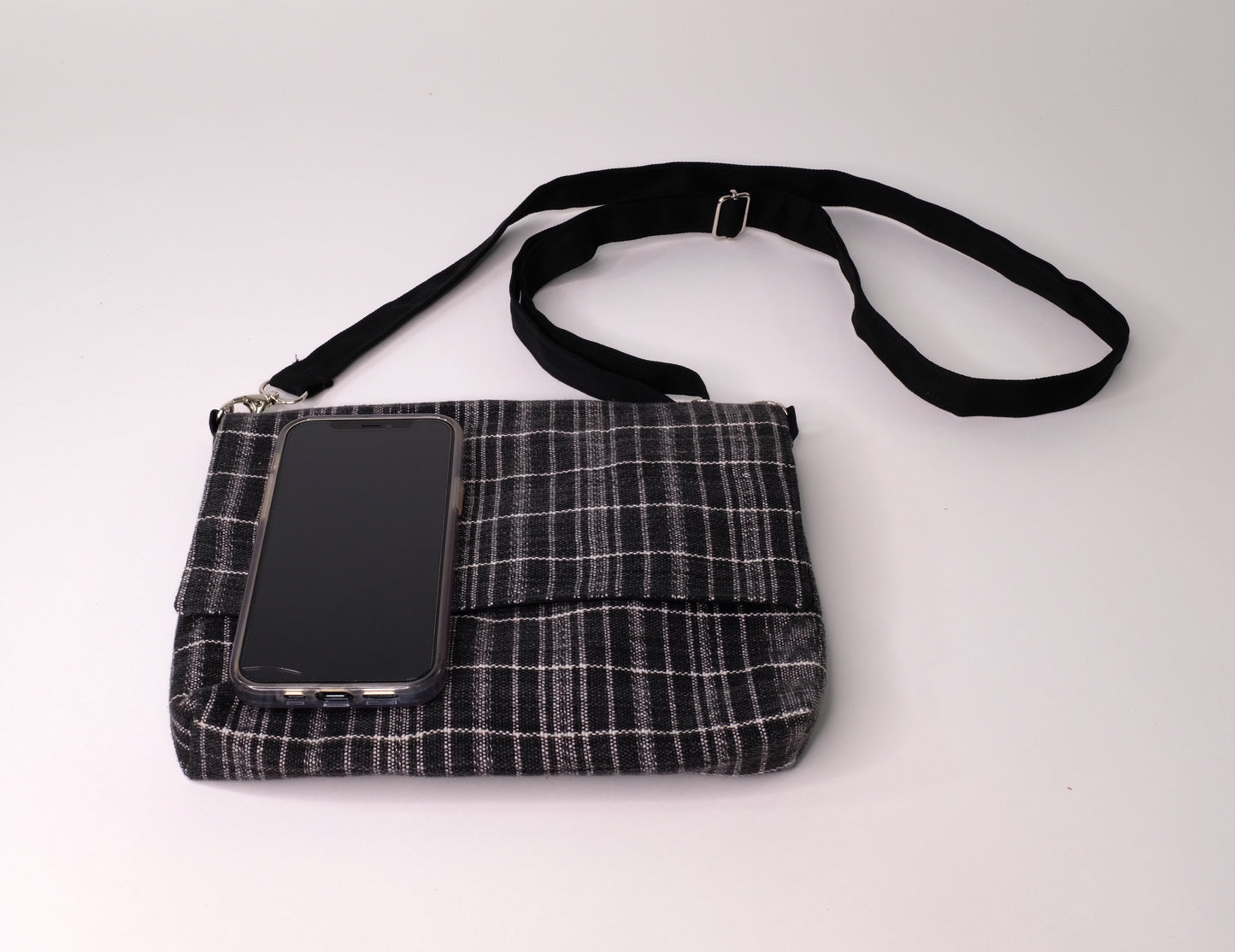 Crossbody bag constructed with carefully handwoven black ikat cotton textiles. With a phone for size comparison.