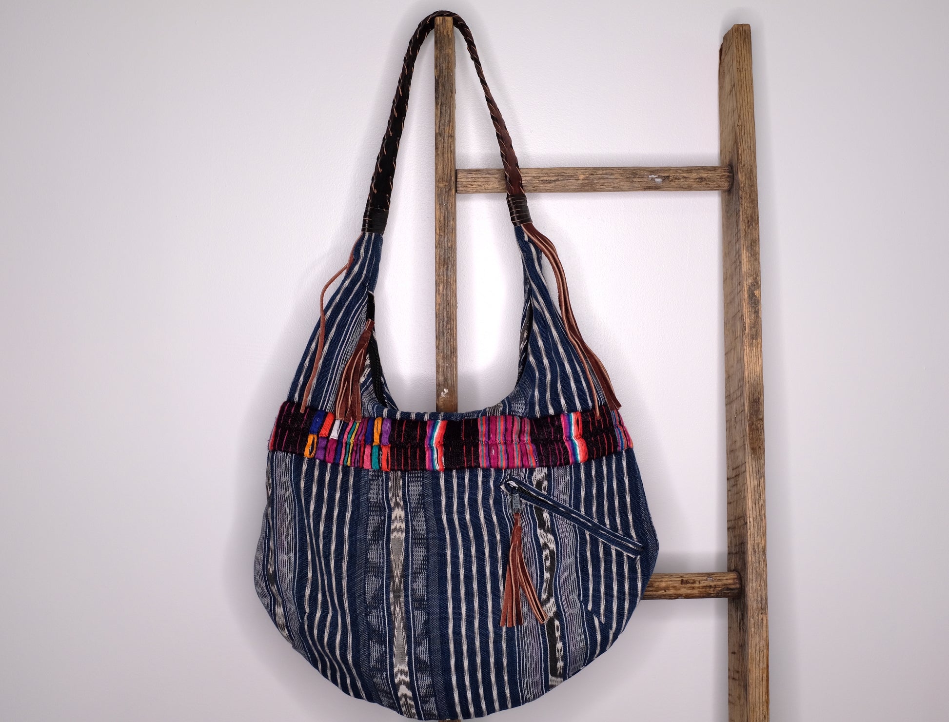 Blue handbag made with recycled Guatemala textiles, embroidery and leather fringe. Hanging on a ladder.